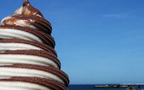 Schoko-Vanille-Eis (weiß und braun, gedreht, Softeis) vor dem blauen Meer.